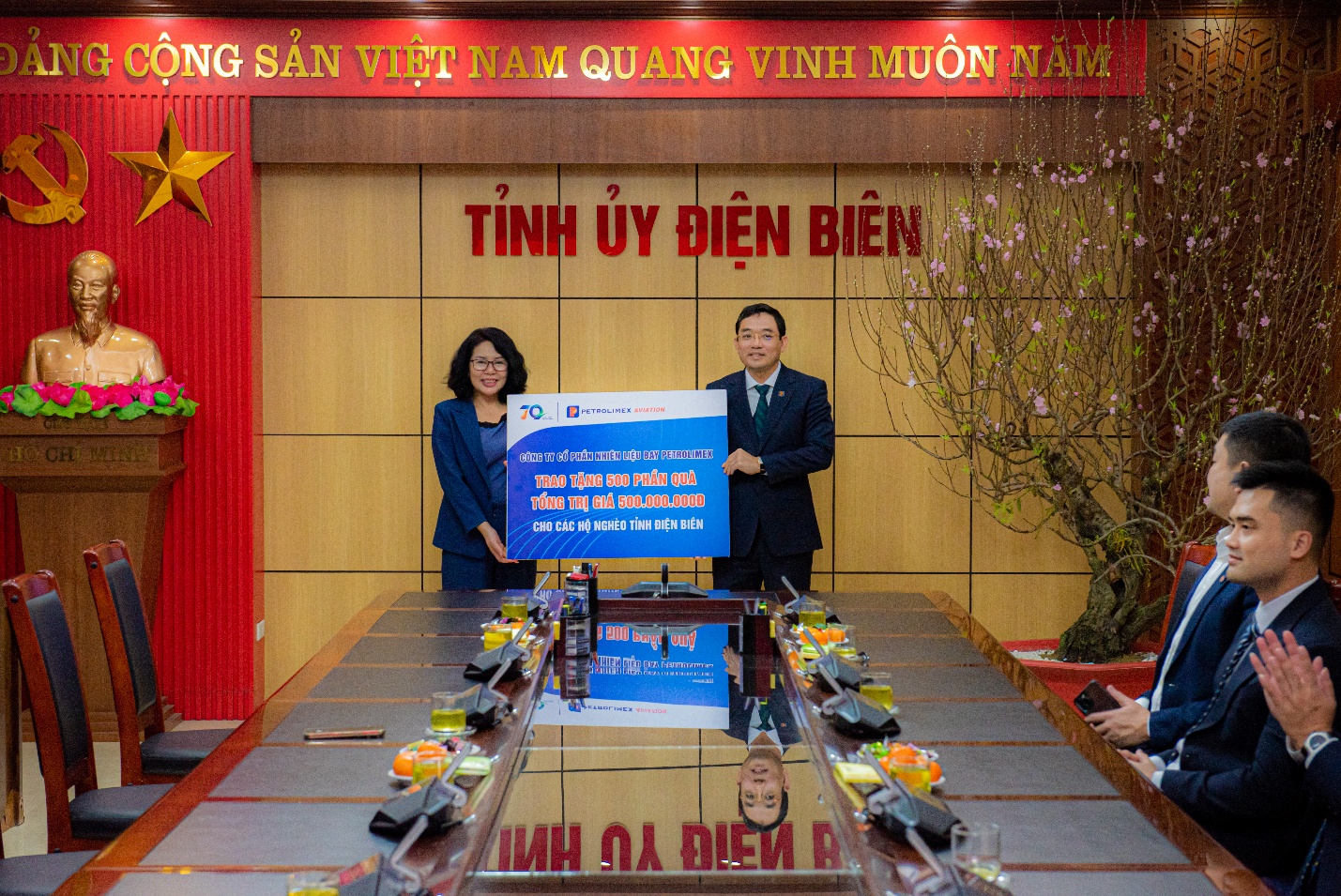 A person and person standing in front of a table with a signDescription automatically generated