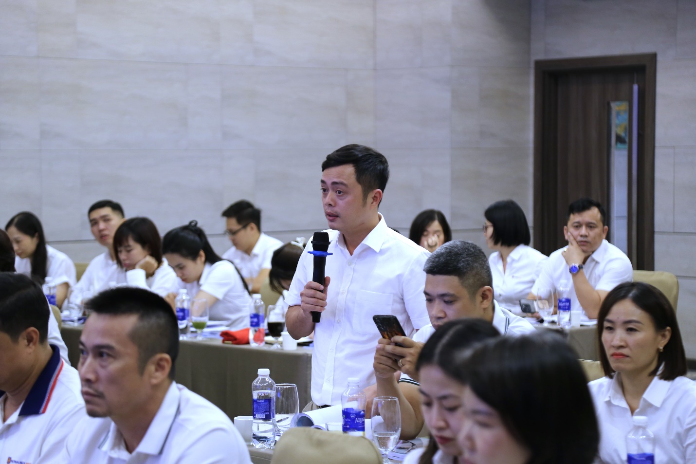 A person speaking into a microphone in a room with people sitting aroundAI-generated content may be incorrect.